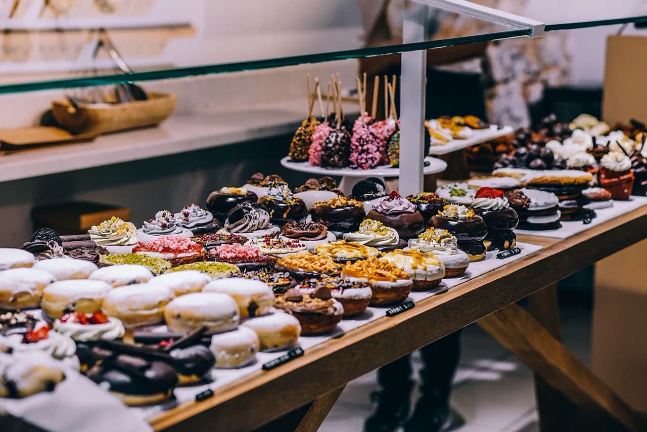 Bir pastane vitrininde ahşap tezgâh üzerinde sıra sıra dizilmiş çeşitli soslu donutlar ve tatlılar