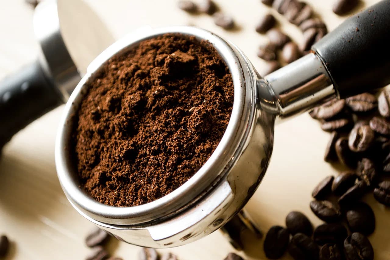 Kahve çekirdeklerinin arasında, taze çekilmiş kahveyle dolu bir espresso makinesi portafiltresi