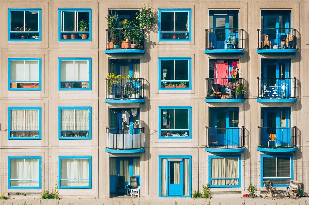 Mavi çerçeveli pencereleri ve saksı bitkileriyle dolu balkonlarıyla bej renkli bir apartman cephesi